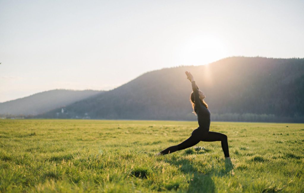 nguoi phu nu tap yoga tren canh dong xanh voi nui xa